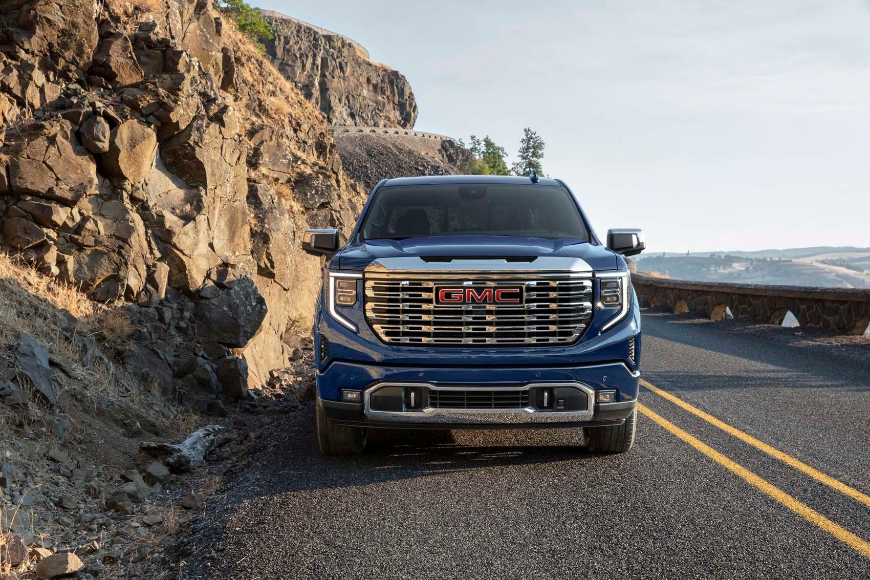 Blue GMC Sierra 1500 traveling on a paved road with hilltops on the side and in the background